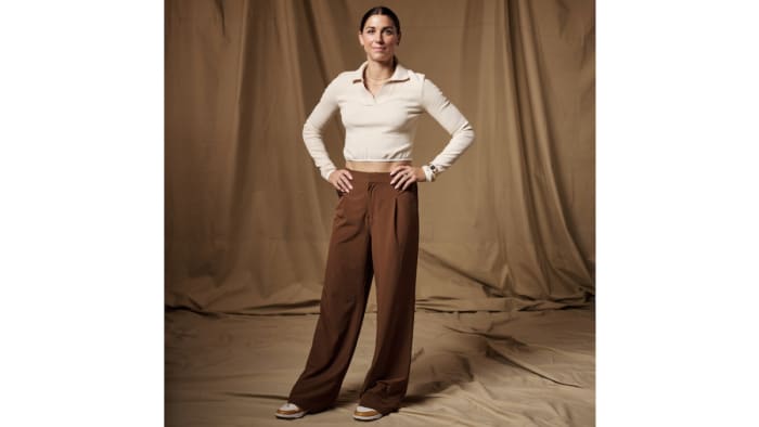 Alex Morgan poses in brown pleated pants and a long-sleeve cream-colored top.